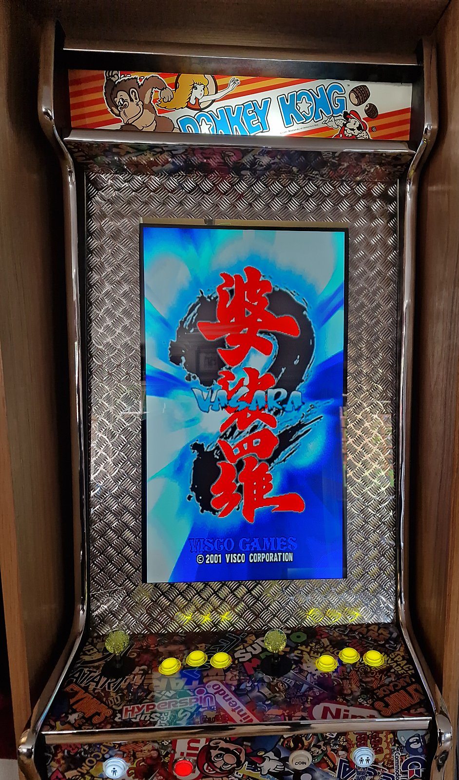 Bartop vertical arcade machine with chequer-plate bezel, chrome trim, sticker-bomb artwork and illuminated buttons